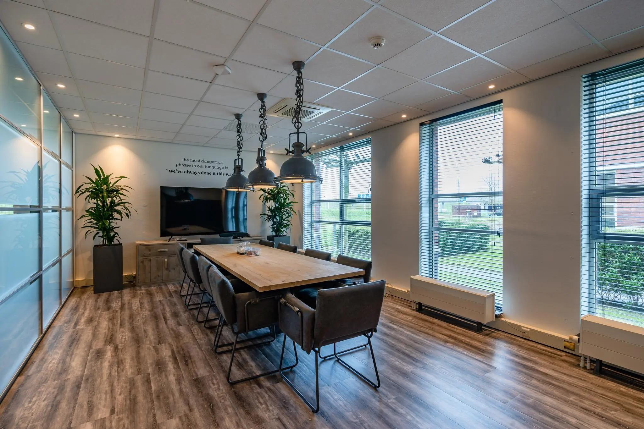 Vergaderruimte aan de 1e Barendrechtseweg met een lange houten tafel, industriële lampen en grote ramen met jaloezieën.